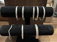 Eight sterling silver bangle bracelets displayed on black velvet stands. Five bangles are plain bands, three have patterns.