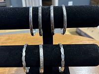 Seven sterling silver bangle bracelets on a black display stand, showing four plain bands with tarnish and three patterned bands.