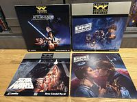 Four Star Wars LaserDiscs and an Empire Strikes Back soundtrack album arranged on a floor, showing cover artwork of Star Wars movies with logos and images of characters.