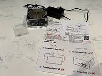 Full view of Tesla coil device with instruction sheet and power adapter laid out on countertop.