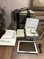 Photo showing the beige Macintosh carrying bag, external floppy drives, manuals, and glare guard laid out on table