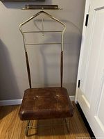 Front view of vintage valet stand with cushioned brown seat, metal and wooden frame with brass elements.