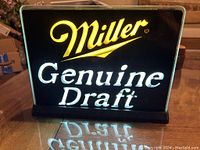 Front view of lighted Miller Genuine Draft sign showing illuminated text and black base.
