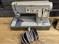 Vintage Singer Zig Zag Model 457 sewing machine showing front and left side with controls and brand logo and attached power cord and pedal.