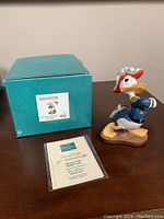 Photo showing Donald Duck sculpture, turquoise box with label, and Certificate of Authenticity.