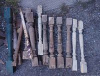 Lot of 11 antique wooden staircase spindles laid on gravel surface showing various paint colors and wear.