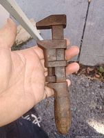 Photo of antique plumbers wrench held in hand showing metal and wood handle with visible rust and wear.