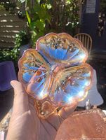 Handheld photo showing the iridescent orange carnival glass shamrock clover dish reflecting sunlight with a sparkling effect.