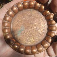 Copper plate held in hand showing scalloped edge and floral engraving with patina and green oxidization spots