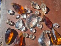 Image showing assorted clear and amber faceted crystals of different shapes and sizes including teardrops, rounds, and ovals, laid out on a wooden surface.