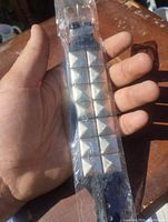 Close-up photo of black leather bracelet with two rows of metal pyramid spikes held in hand, showing texture and detail.