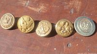 Front view of five military and police buttons laid in a row showing varying insignias.