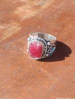Close-up photo of the silver plated ring showing the large natural ruby stone and silver decorative elements on the band, laying on a wooden surface.