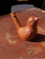 Side angled view of the red clay pottery bird whistle showing detailed textured feathers and beak-shaped mouthpiece.