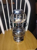 Front view of vintage glass coffee percolator showing upper and lower glass chambers and metal base with handles.