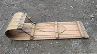 Side angle view of vintage wooden toboggan sled showing curled front end and rope handles.