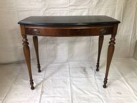 Full front view of antique wooden desk showing curved drawer front, brass handles, and intricately turned legs on all four corners.