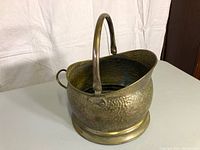 Angled view of antique brass bucket showing hammered texture and curved handle