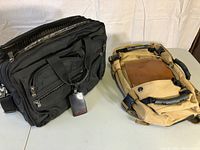Black Tumi work bag and tan canvas bag shown side by side on a surface.