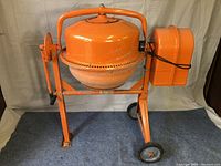 Front view of the orange cement mixer showing motor housing and mixing drum.