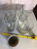 Five different glass vases arranged on a table with measuring tape showing size reference.
