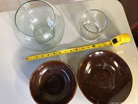 Two clear glass bowls and two brown ceramic bowls with tape measure for scale on white table
