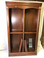Front view of the large wooden bookshelf showing the two main vertical sections, decorative top molding, and the stacked wooden shelves inside.