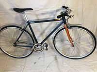 Side view of Scattante Americano singlespeed road bike showing blue frame, orange fork, wheels, chainring, pedals, and seat.