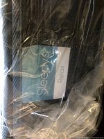 Close-up photo of the Sleepys mattress label showing brand and model 'Relax', wrapped in clear plastic.