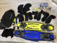 Photo showing two sets of snorkeling gear including fins in yellow and blue, snorkels, masks, gloves, boots, and carrying bags.