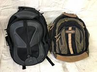 Two backpacks side by side; black backpack with molded padded front and green Timberland backpack with tan base and accents