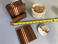 Photo showing wooden coasters with striped inlay, ceramic coaster holder with natural stone pattern, round ceramic coaster and measuring tape for size reference.