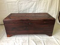 Front view of rectangular wooden chest with dark reddish finish, sitting on fabric background.