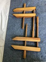 Photo showing three light wood clamps with threaded wooden screws for clamping, laid out on a grey carpeted surface.