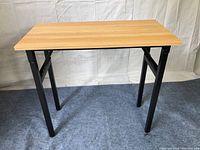 Rectangular wooden table with metal black folding legs set up on carpet, good condition and sturdiness visible.