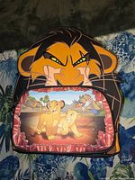 Front view of The Lion King themed Loungefly backpack showing Simba, Nala, Zazu, and Scar artwork.