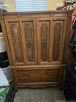 Closed view of the Gothic style armoire showing ornate carved wood doors with metal ring pulls and two large drawers below with decorative metal handles.