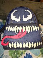 Front view of Loungefly backpack with Venom design including eyes, teeth, and tongue in blue faux leather.