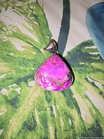 Front view of the triangular rhodochrosite crystal pendant with vibrant pink and purple hues set in silver.