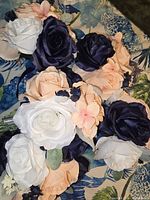 Close-up photo showing a cluster of navy blue, white, and peach artificial flowers including roses and smaller blossoms, resting on floral patterned fabric.