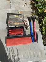 All items laid out on concrete showing warning triangle kits, ice scrapers, hooks, small container, and cable.