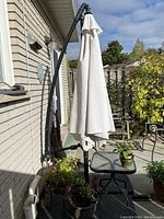 Closed beige umbrella on curved offset stand against house wall