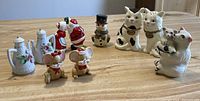 Nine pairs of ceramic salt and pepper shakers with Christmas, cat, Mum & Baby, and coffee pot designs arranged on a wooden table.