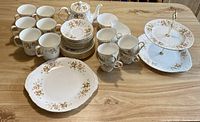 Full view of the vintage Colclough bone china tea set items arranged on wooden table showing all pieces including plates, mugs, cups, teapot, and tiered cookie plate.