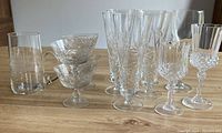 Photo of 13 vintage crystal glasses set on wooden surface, showing small glasses, beer glasses, and wine glasses with pinwheel cut pattern.
