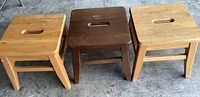 Front view of three wooden stepstools side by side, two light wood and one dark wood in the middle, showing overall shape and style.