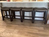 Four black painted wood frame stools with grey upholstered seats lined up at a counter, side view