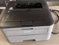 Front angle view of the Brother HL-L2320D printer showing the paper output tray and power cable.