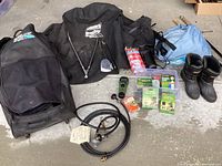 Overview of the lot showing the blue Coleman propane grill in wheeled case, black BBQ cover, women's winter boots, fishing walking sticks, and other items on concrete floor.