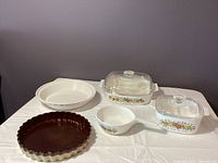 Overview of all items: two Corningware dishes with lids, a ceramic quiche pan, a ceramic pie pan, and a Corningware saucepan with handle